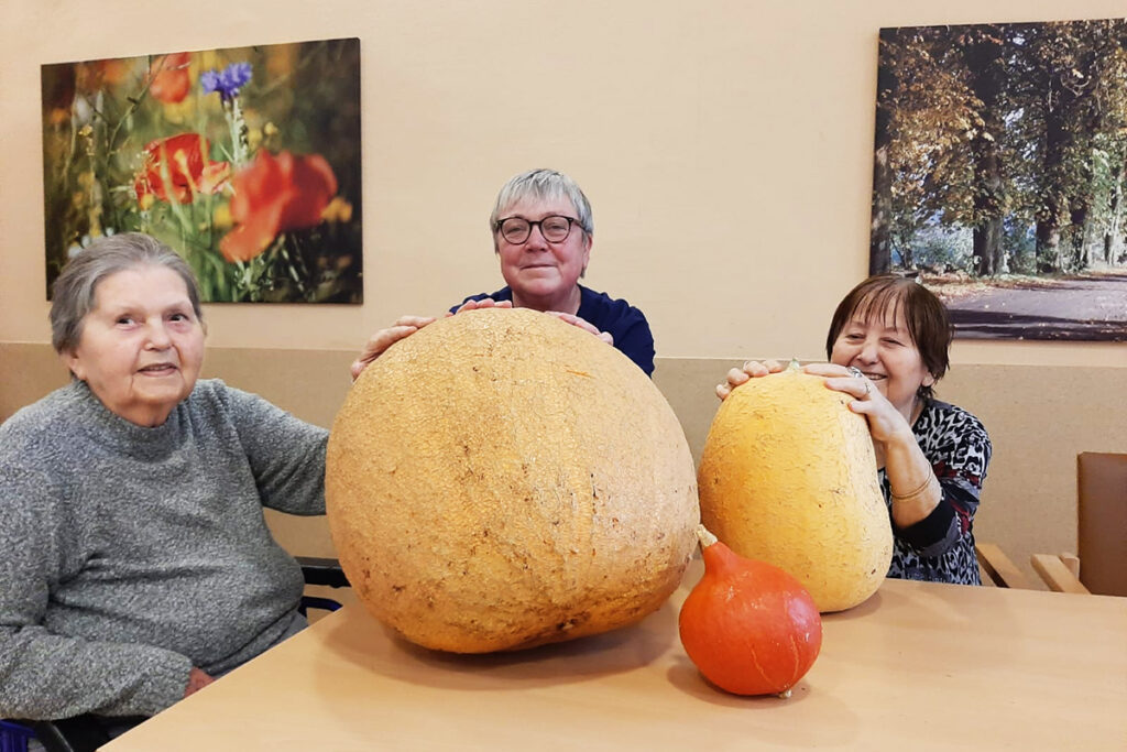 Drei Personen sitzen an einem Tisch mit gro&szlig;en K&uuml;rbissen.