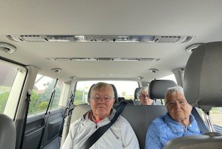 Drei ältere Personen sitzen auf den Rücksitzen eines Autos.