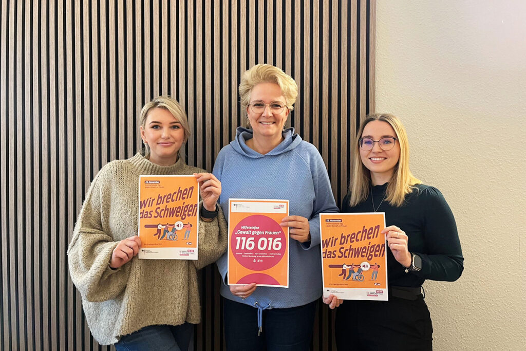 Drei Personen halten Plakate in den Händen.