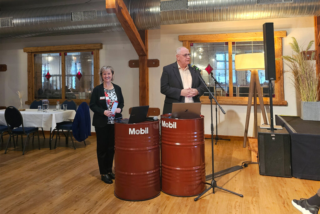 Zwei Personen pr&auml;sentieren in einem Raum vor einem Mikrofon.