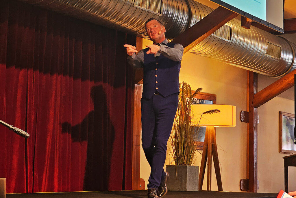 Ein Mann auf einer B&uuml;hne in einem Raum mit rotem Vorhang und gelber Beleuchtung.