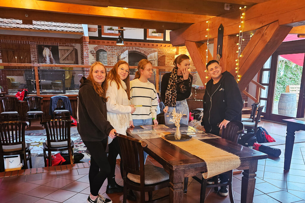 F&uuml;nf Personen posieren gemeinsam in einem gem&uuml;tlichen Innenraum.