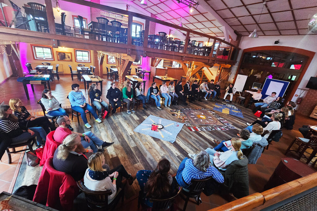 Menschen sitzen im Stuhlkreis in einem gro&szlig;en Raum