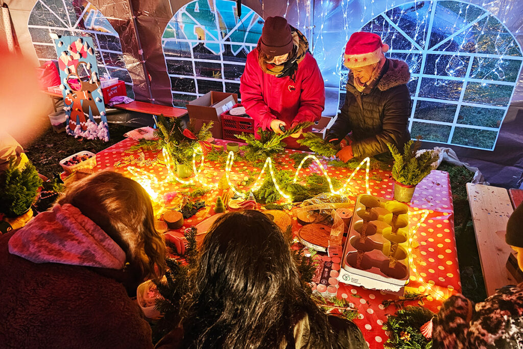 Menschen gestalten Weihnachtsdekorationen an einem Tisch mit Lichterketten