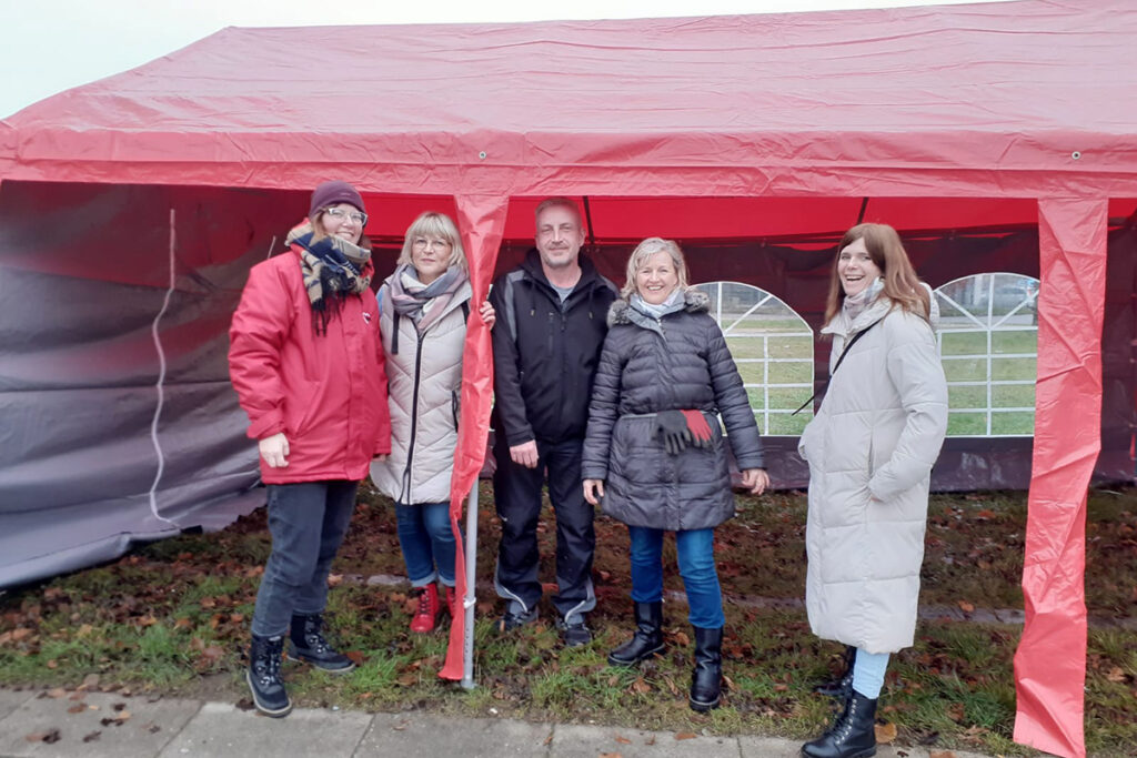 Fünf Personen stehen vor einem roten Pavillon im Freien.