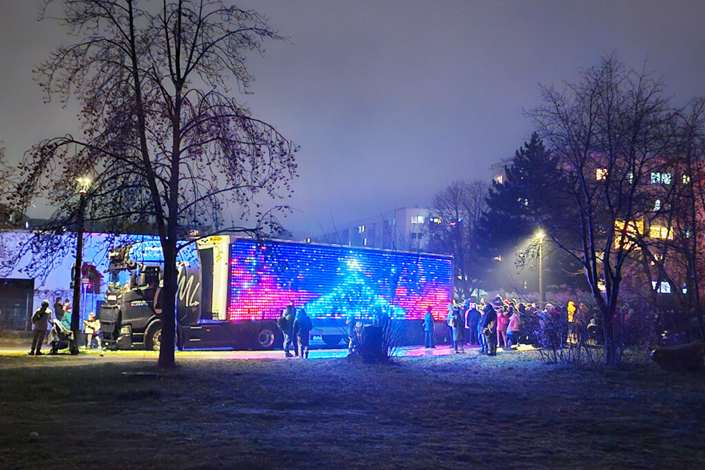 Ein bunt beleuchteter LKW mit Menschen, die sich im Freien darum versammeln.
