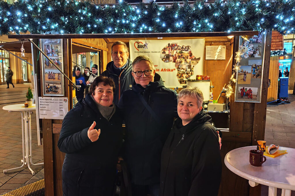 Vier Personen stehen vor einem weihnachtlich dekorierten Stand mit AWO-Logo und einer Karte Afrikas.