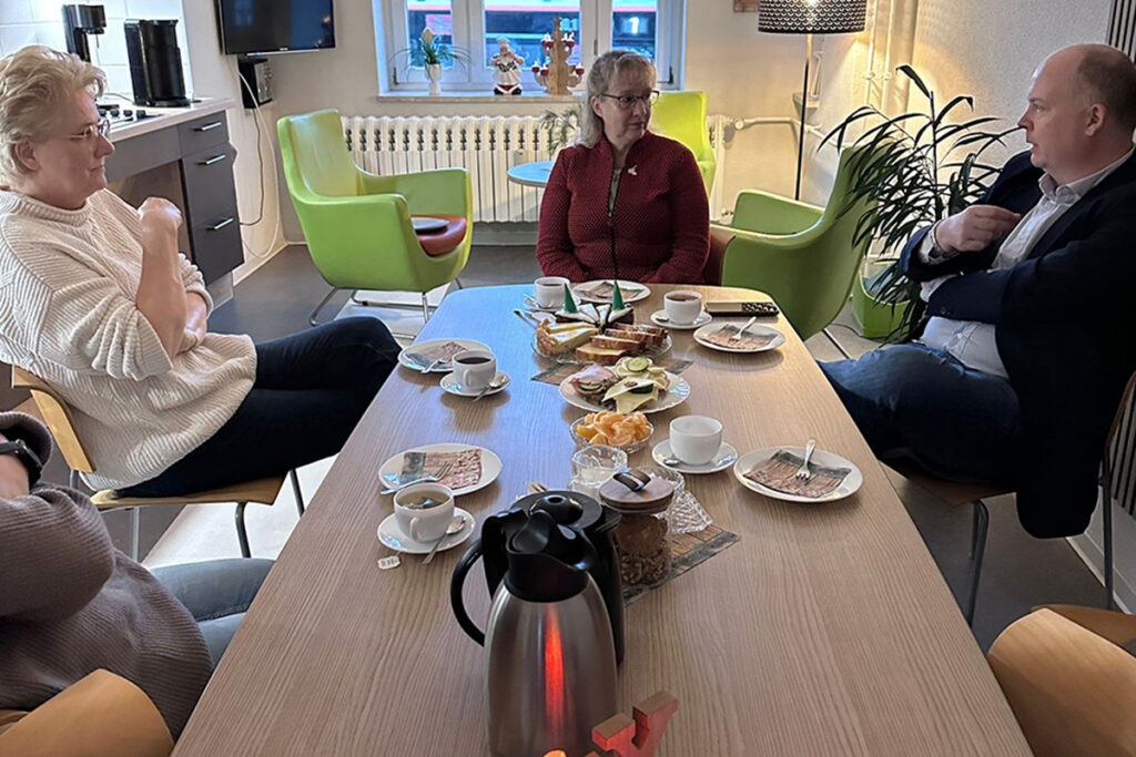 Mehrere Menschen sitzen an einem Tisch mit Geb&auml;ck und Getr&auml;nken.