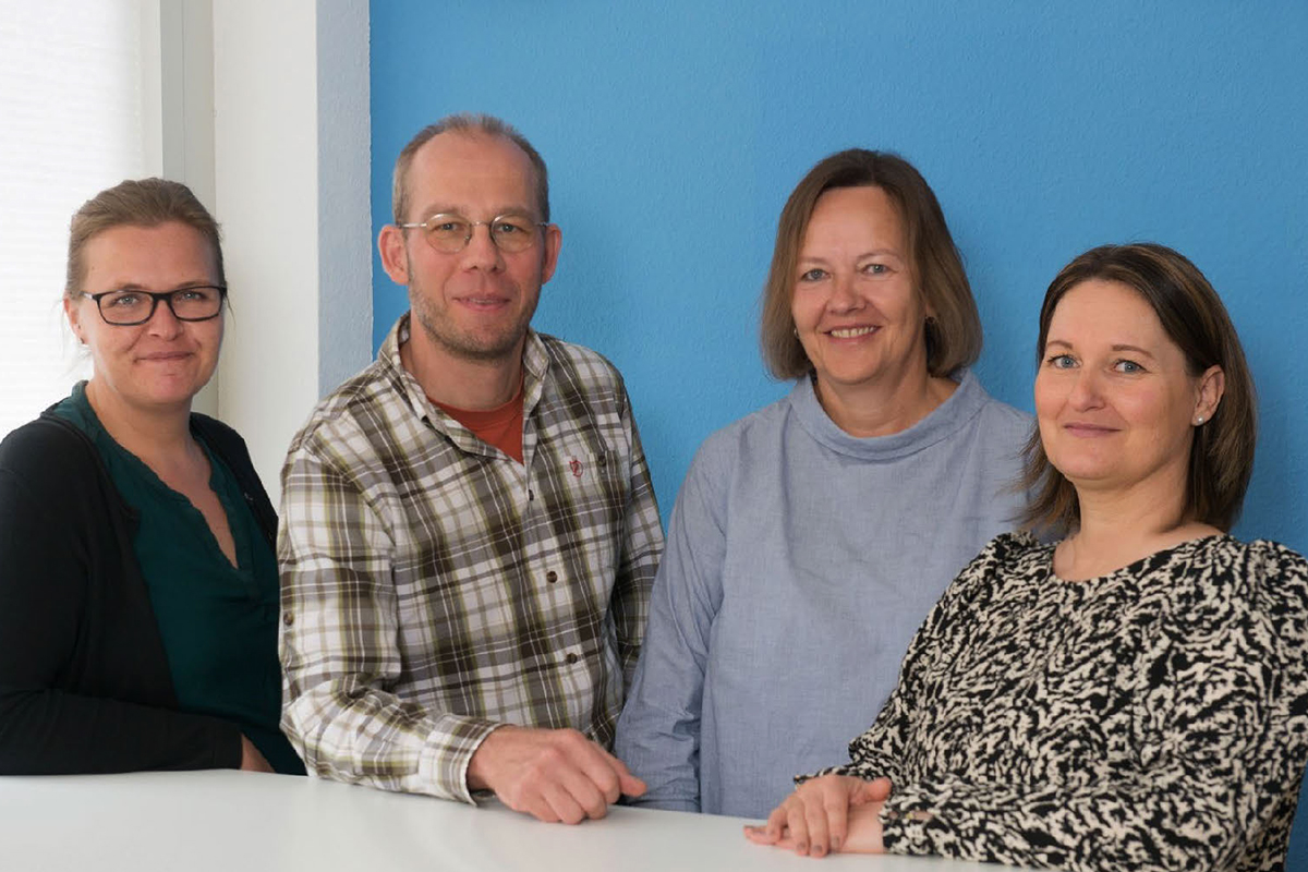 Vier Personen stehen nebeneinander vor einer blauen Wand.
