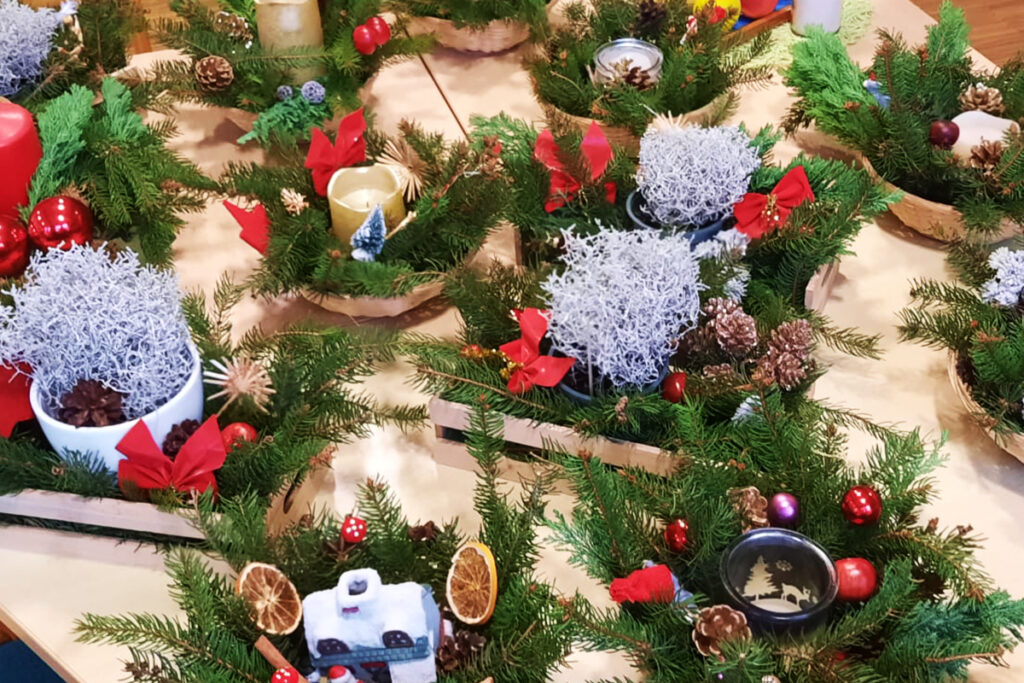 Weihnachtliche Gestecke mit gr&uuml;nen Zweigen, roten Kerzen und Dekoration.