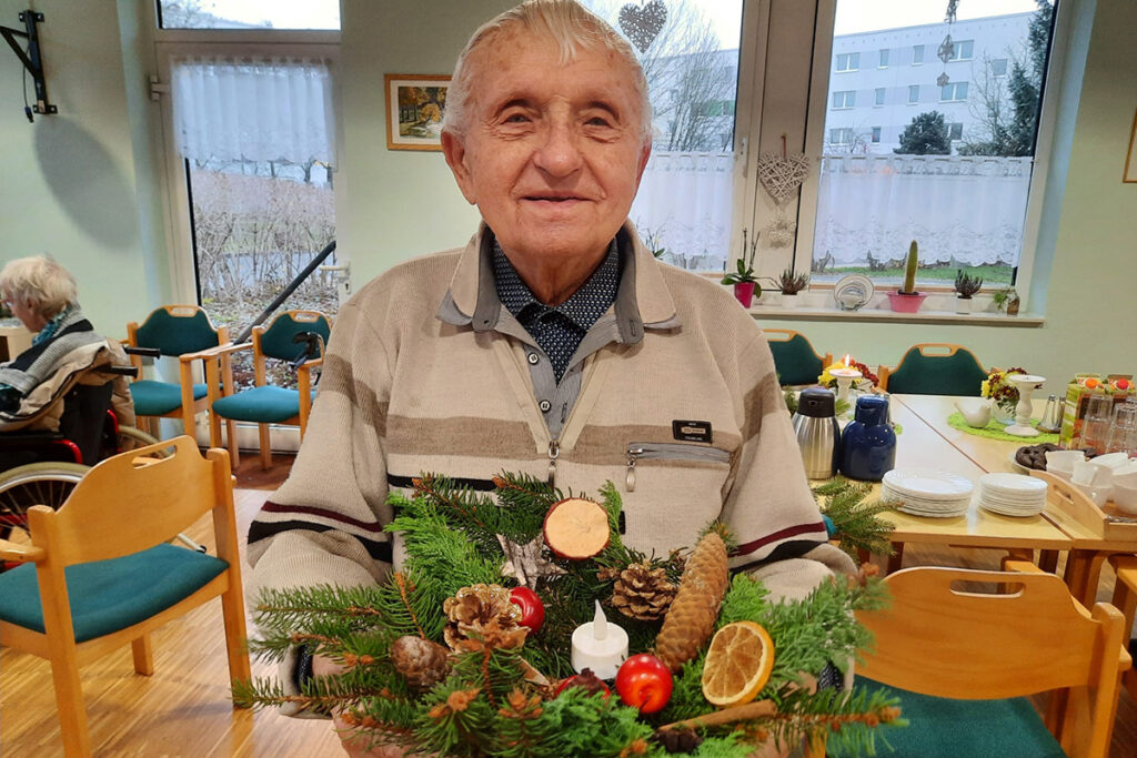 Ein &auml;lterer Mann h&auml;lt einen Adventskranz in den H&auml;nden.