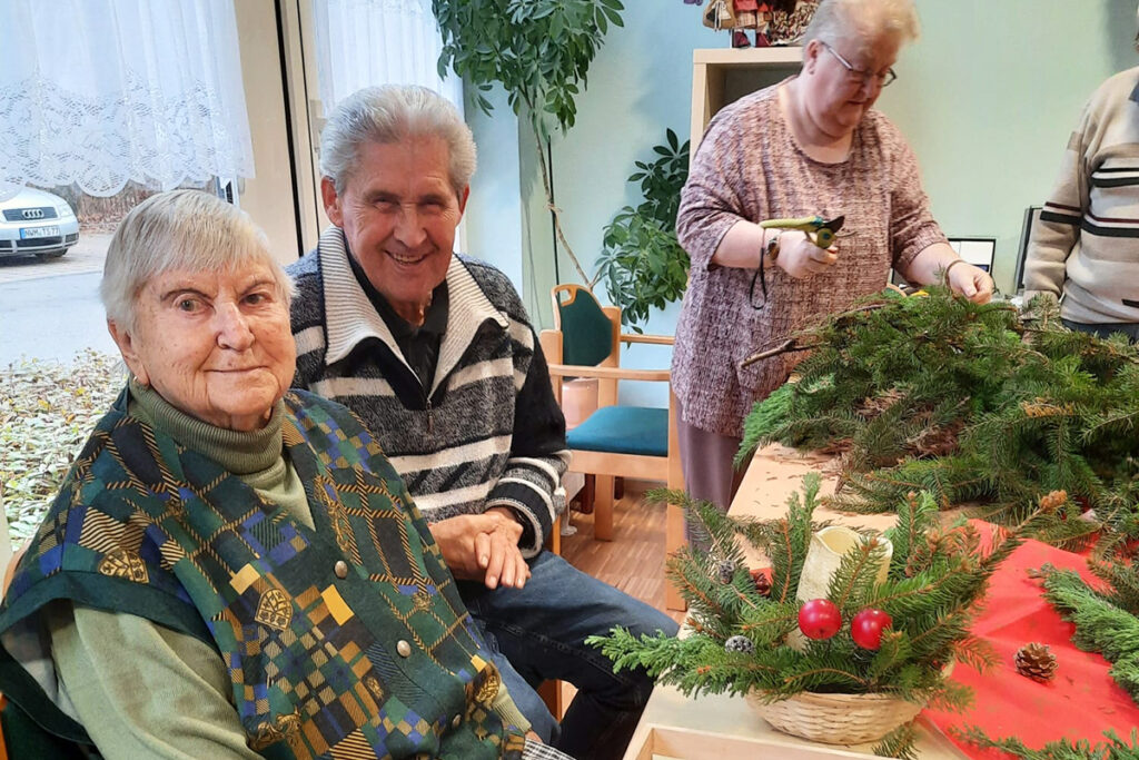Drei Personen sitzen und stehen um einen Tisch mit Tannenzweigen.