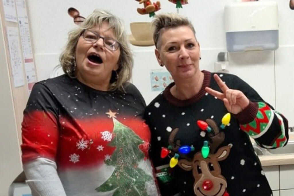 Zwei Frauen in weihnachtlichen Pullovern stehen nebeneinander in einem Raum.