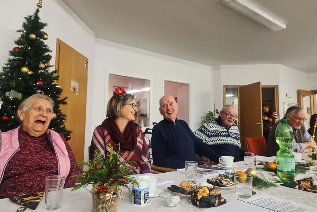 Eine Gruppe &auml;lterer Menschen sitzt lachend an einem festlich gedeckten Tisch.