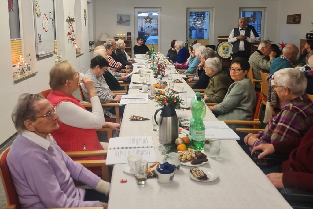Menschen sitzen in einem Raum an einem langen Tisch, Getr&auml;nke und Snacks sind auf dem Tisch