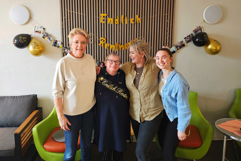 Gruppe von vier Frauen bei einer Feier, vor einer Wand mit Dekoration für den Ruhestand.