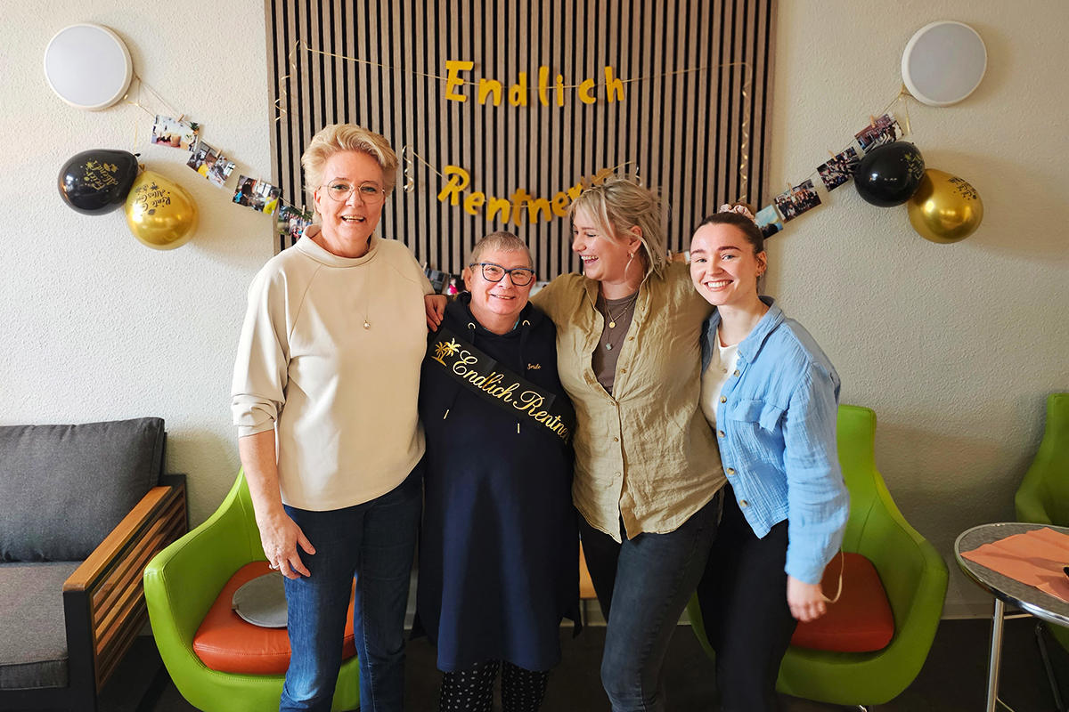 Gruppe von vier Frauen bei einer Feier, vor einer Wand mit Dekoration für den Ruhestand.