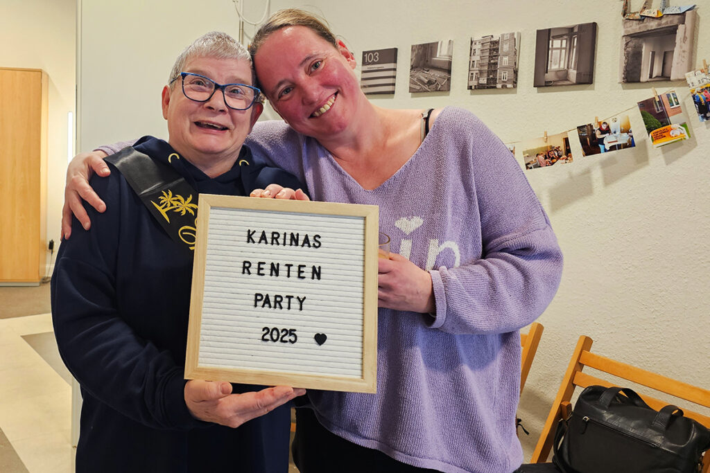 Zwei Personen halten ein Schild mit der Aufschrift 'Karinas Renten Party 2025' und l&auml;cheln in die Kamera.