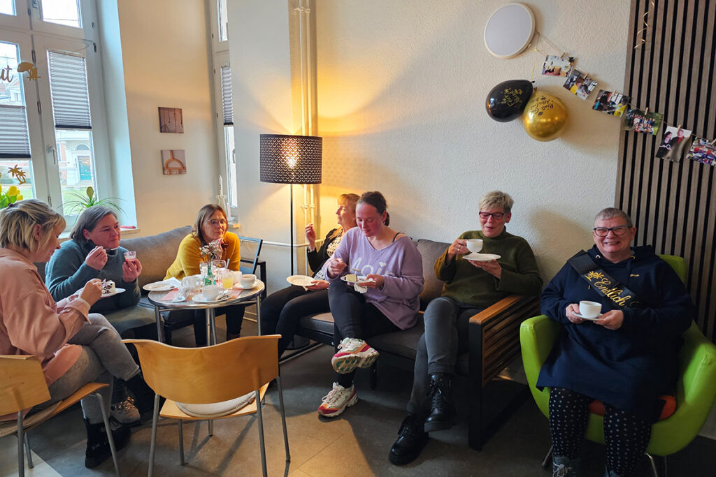 Mehrere Personen sitzen in einem gem&uuml;tlichen Raum und trinken Kaffee.