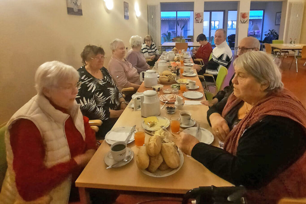 Eine Gruppe &auml;lterer Menschen sitzt an einem langen, gedeckten Tisch und isst zusammen.