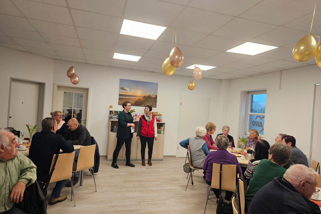 Ein Gemeinschaftsraum mit mehreren Menschen, die an Tischen sitzen und sich unterhalten.