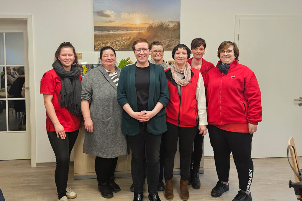 Gruppe von sieben Frauen posiert l&auml;chelnd f&uuml;r ein Foto in einem Innenraum.