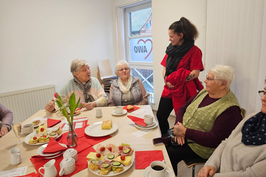 Mehrere &auml;ltere Damen sitzen an einem Tisch mit einer jungen Frau im Gespr&auml;ch.
