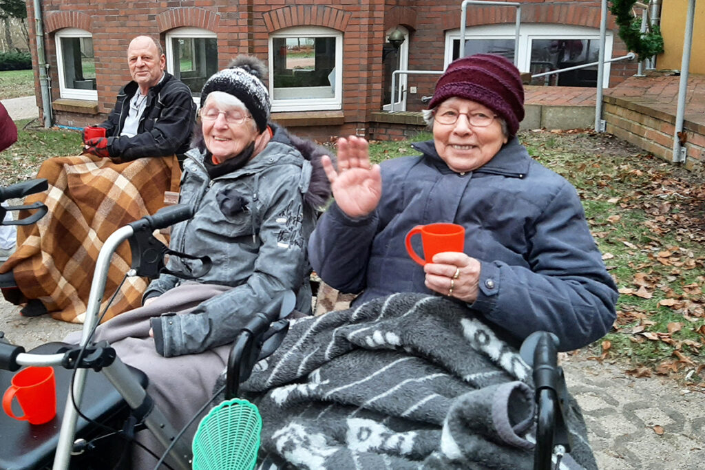 Ältere Menschen draußen sitzend, warm eingepackt und lächelnd.