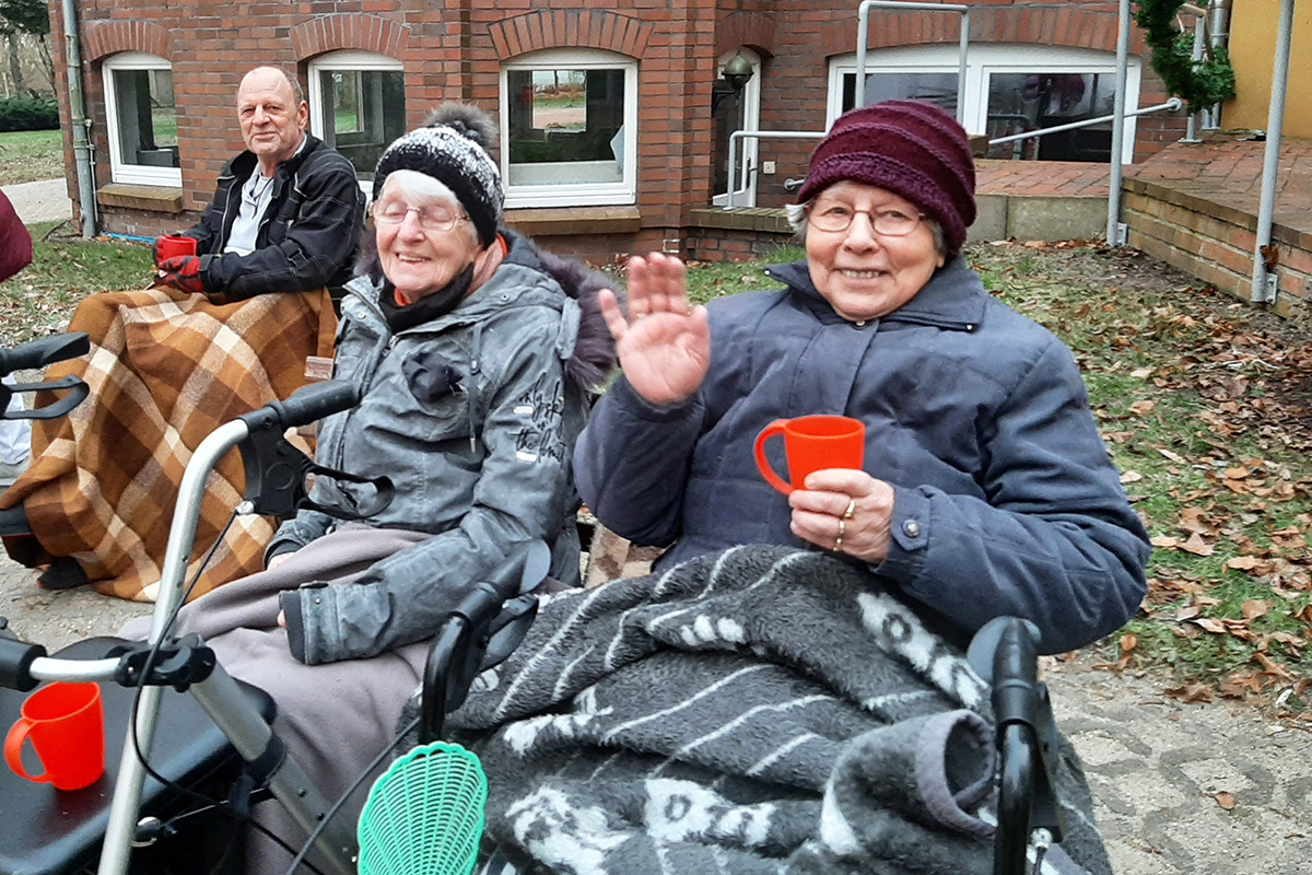 Ältere Menschen draußen sitzend, warm eingepackt und lächelnd.