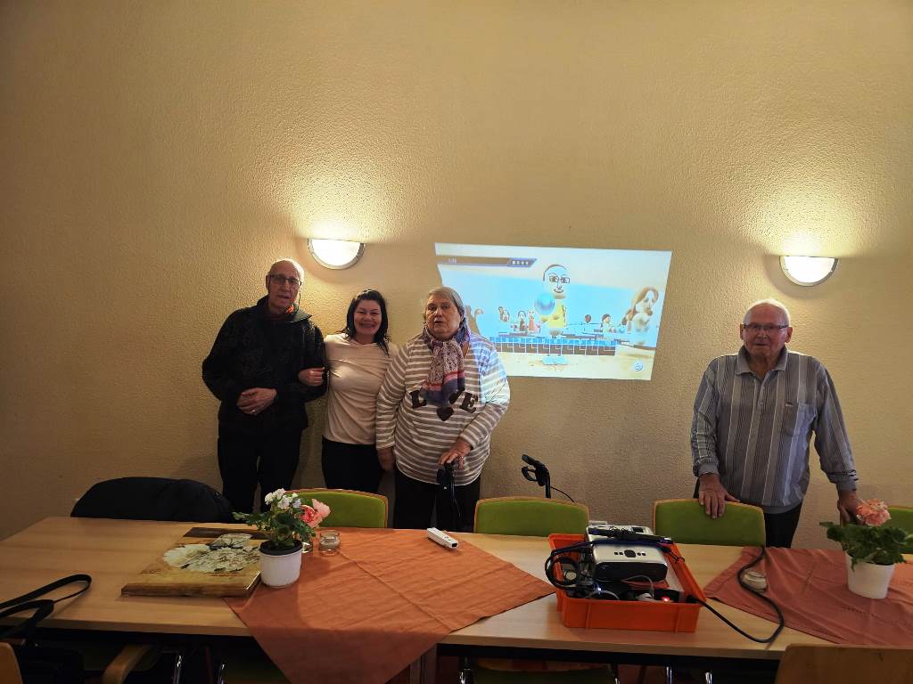 Vier Menschen stehen in einem Raum vor einer Projektion, die eine Animation zeigt.