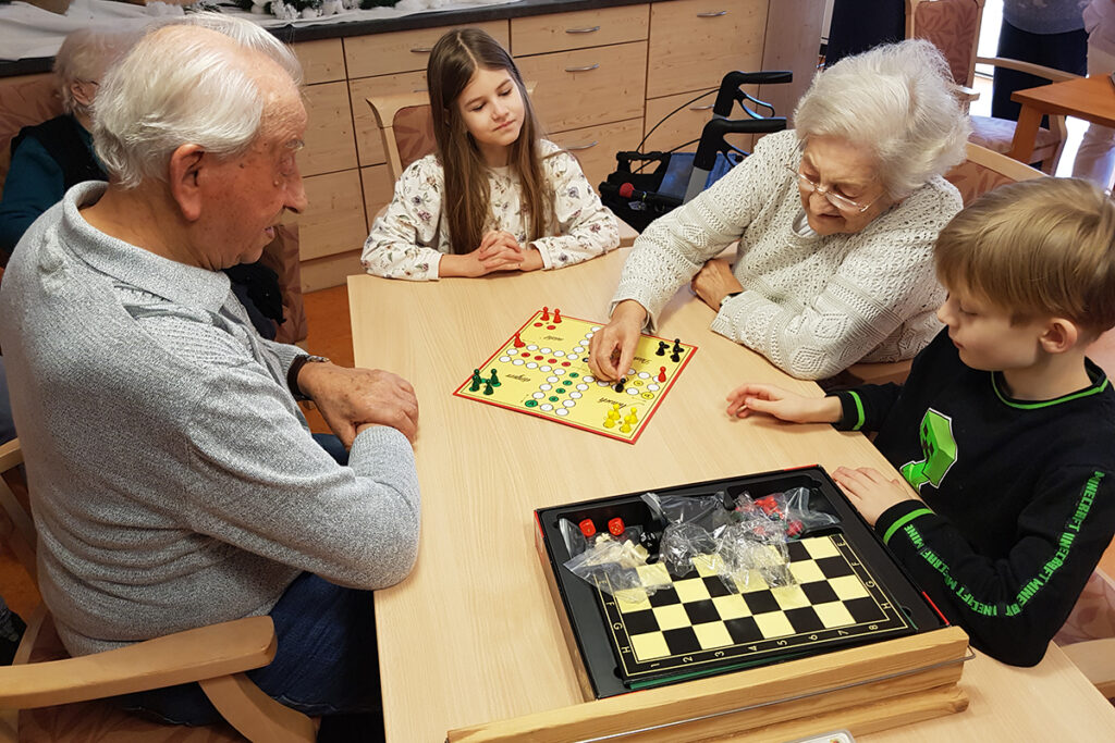 Menschen unterschiedlichen Alters spielen gemeinsam ein Brettspiel an einem Tisch.