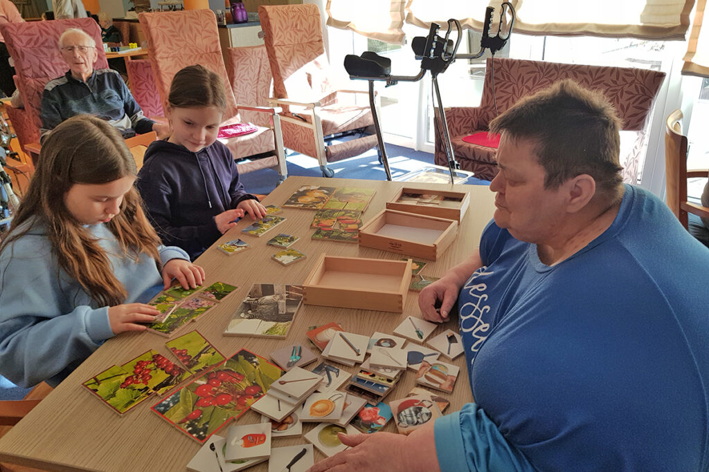 Gruppe von Menschen spielt Brettspiel an einem Tisch in einem Gemeinschaftsraum.