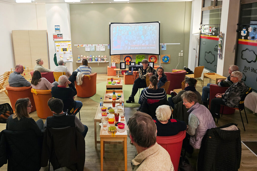Menschen bei einer Veranstaltung in einem Raum mit Projektionsleinwand.