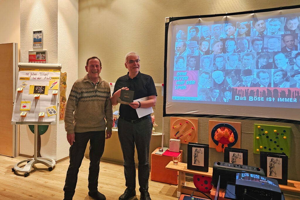 Zwei M&auml;nner stehen l&auml;chelnd vor einer Pr&auml;sentationsleinwand.