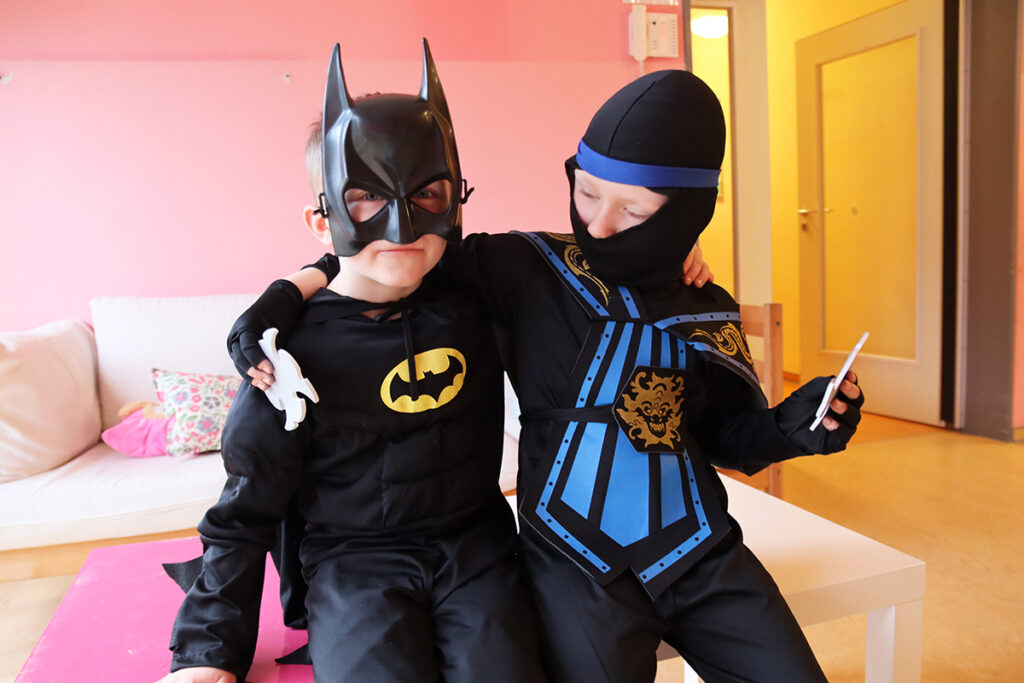 Zwei Kinder in Superheldenkost&uuml;men sitzen auf einem Tisch.