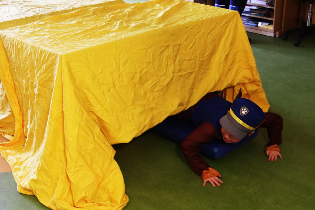 Kind kriecht unter gelbem Tuch hindurch