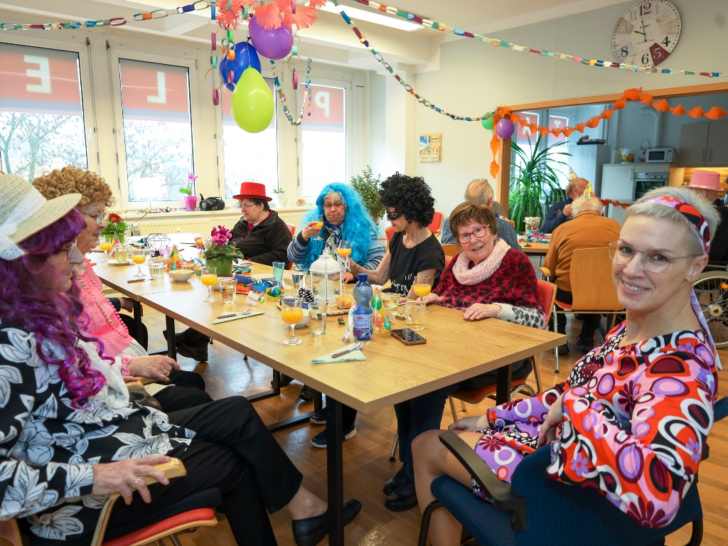 Eine Gruppe älterer Menschen feiert Fasching in einem Gemeinschaftsraum