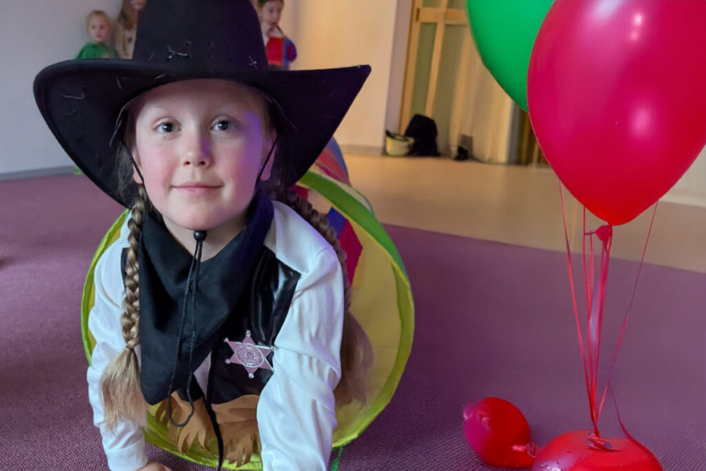 Ein Kind in einem Cowboy-Kost&uuml;m mit schwarzem Hut und Westernstern l&auml;chelt in die Kamera.