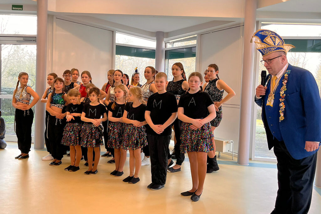 Eine Gruppe von Kindern und ein Mann in einem festlichen Kostüm stehen in einem Raum.