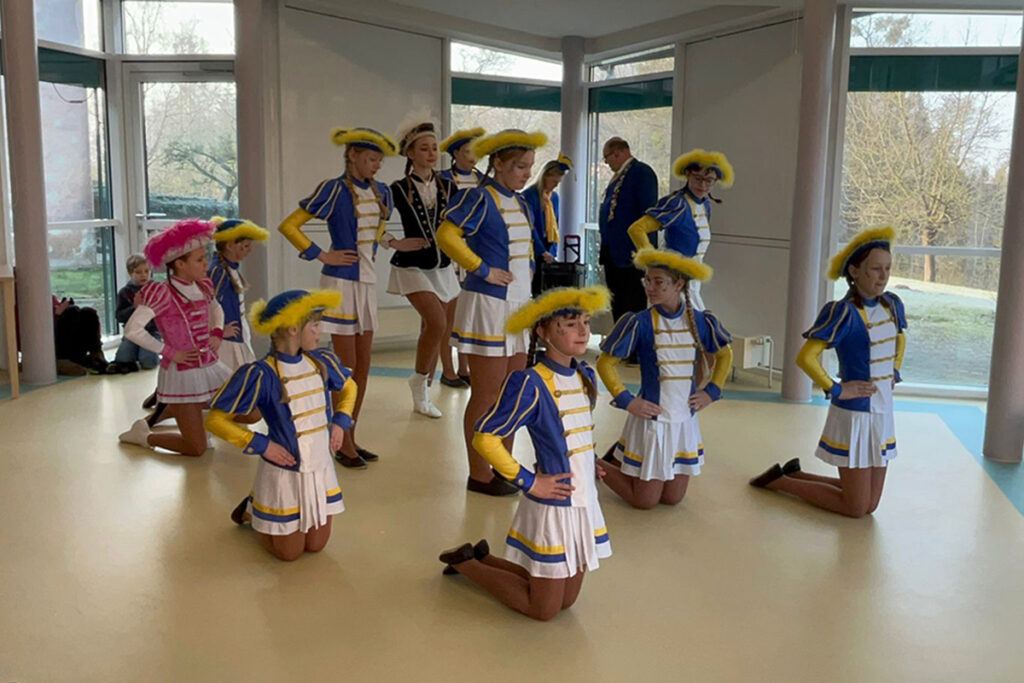 Eine Gruppe junger Personen in bunten Kost&uuml;men kniet und steht in einer Formation.