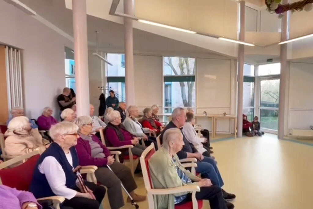 Eine Gruppe &auml;lterer Menschen sitzt in einem hellen Raum auf St&uuml;hlen.