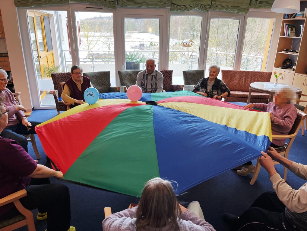 Ältere Menschen mit einem farbigen Schwungtuch in einem Gemeinschaftsraum.
