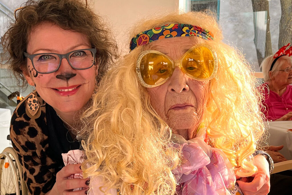 Zwei Menschen in Verkleidung, eine als Katze mit Schminke und eine mit blonder Per&uuml;cke und Sonnenbrille.