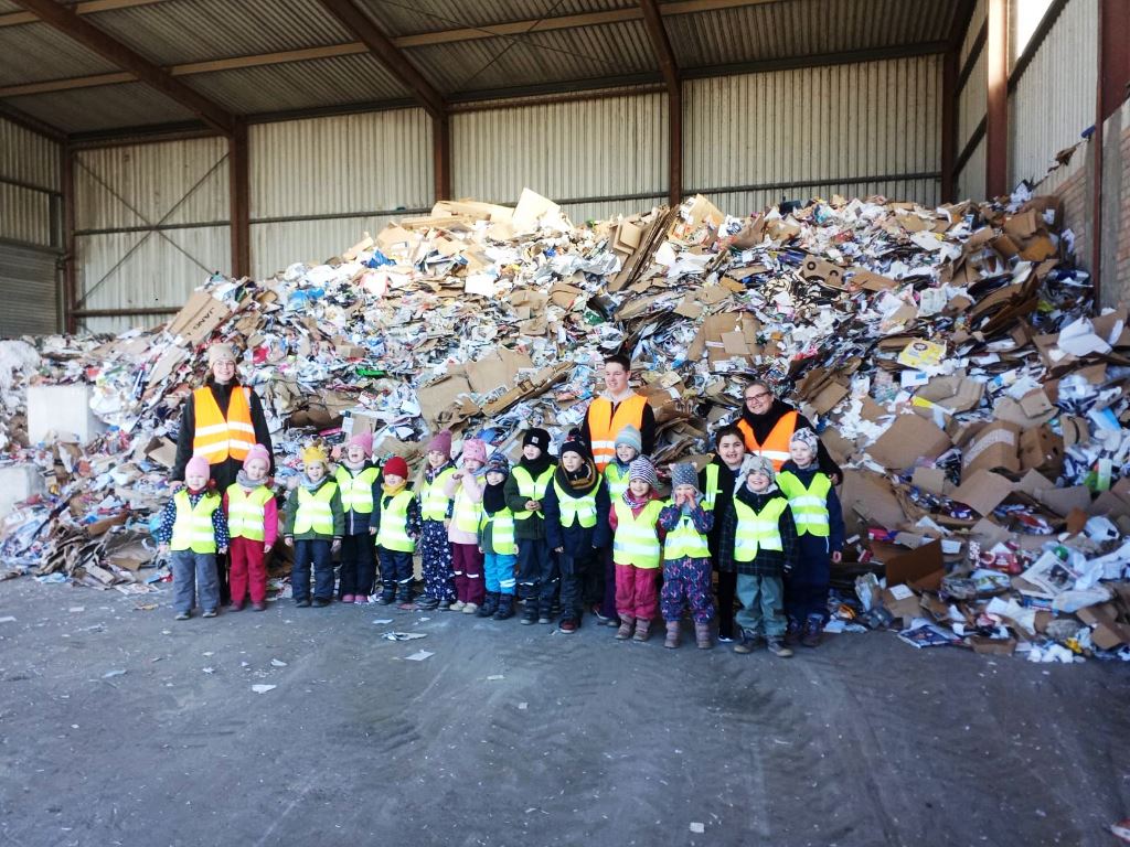 Kinder und Erwachsene in Warnwesten vor einem Papiermüllberg in einer Halle