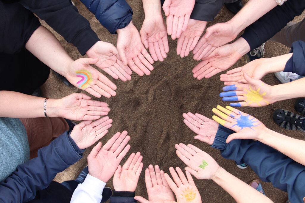 Ein Kreis aus H&auml;nden, die nach oben ge&ouml;ffnet sind, einige mit bunten Bemalungen.