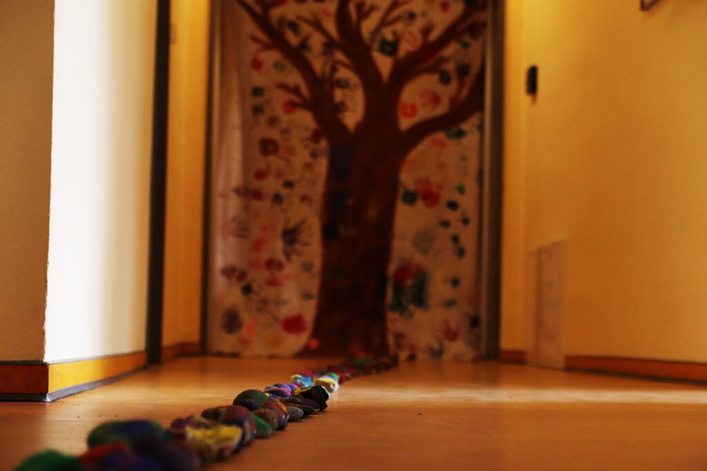 Ein Flur mit einem bunten Steineweg, der zu einer T&uuml;r f&uuml;hrt, an der ein bemaltes Laken mit einem Baum h&auml;ngt.