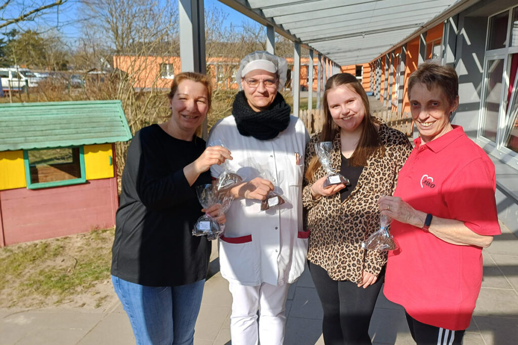 Vier Menschen stehen nebeneinander und halten Geschenke in den H&auml;nden.