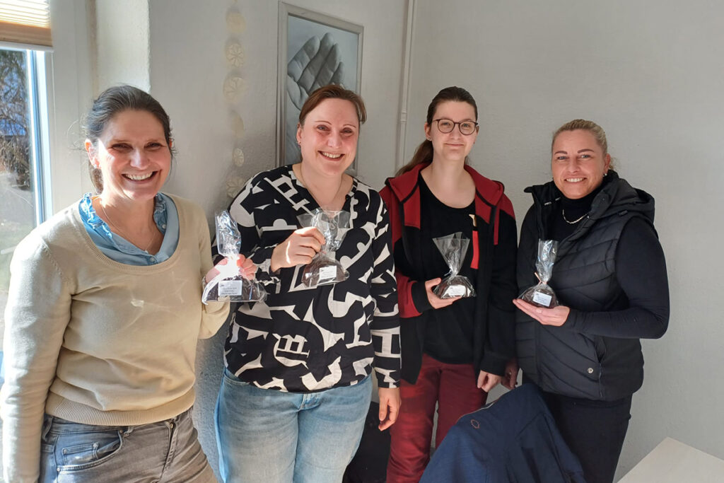 Vier Frauen stehen nebeneinander und halten kleine Geschenkt&uuml;ten.