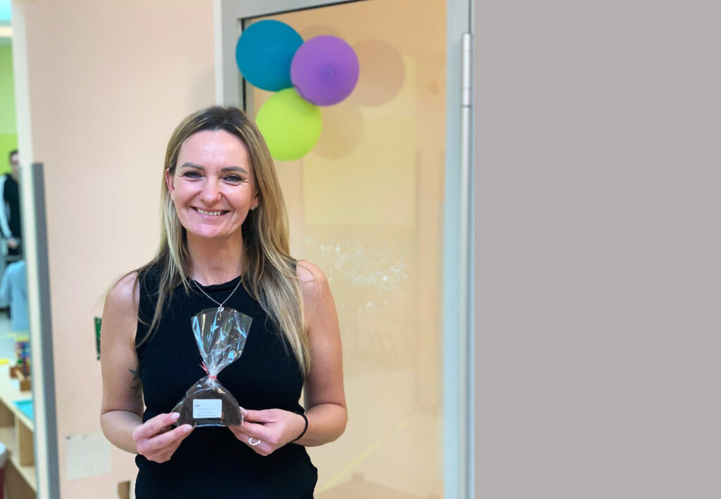 Frau mit Geschenk in der Hand vor Zimmerdekoration mit Luftballons.