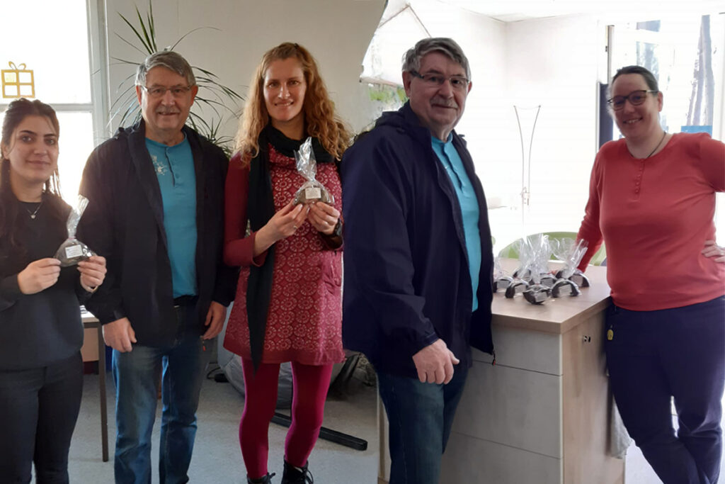 Eine Gruppe von f&uuml;nf Personen steht in einem Raum mit Pflanzen und Geschenkpackungen aus Schokolade.